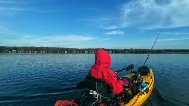 Bir kayıkta oturan balıkçı, elinde kürek tutarken balık yakalamak için gizli bir yere gidiyor. Kano balıkçılığı yarışması. Çevre koruma ve soğuk su için kuru giysili balıkçı..
