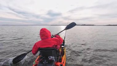 Bir kayıkta oturan balıkçı, elinde kürek tutarken balık yakalamak için gizli bir yere gidiyor. Kano balıkçılığı yarışması. Çevre koruma ve soğuk su için kuru giysili balıkçı..