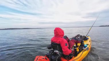 Motorlu bir PDL kanoda oturan balıkçı ve balık yakalamak için gizli noktaya pedal çeviriyor. Kano balıkçılığı yarışması. Çevre koruma ve soğuk su için kuru giysili balıkçı..