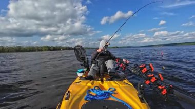 Güneş gözlüklü kapüşonlu balıkçı ve şapkalı balıkçı kano üzerinde küçük panfish yakalayıp bırakıyor. Güneşli bulutlu bir günde gölün ortasında tek başına vakit geçirmek. Bluegill balığı ve balon hattı kamerada.
