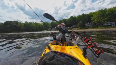 Adam güneşli bir günde gölde kanoyla geziyor. Spor balıkçılığı ve kürek çekme. Erkek turist kanosu, su sporları. Turuncu kano üzerinde balıkçılık turnuvası sırasında suda kürek çeken balıkçı.