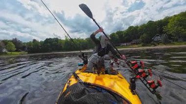 Adam güneşli bir günde gölde kanoyla geziyor. Spor balıkçılığı ve kürek çekme. Erkek turist kanosu, su sporları. Turuncu kano üzerinde balıkçılık turnuvası sırasında suda kürek çeken balıkçı.