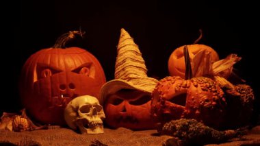 Balkabaklarının Cadılar Bayramı siyah arka planda geçiyor. Cadılar Bayramı ve hasat seti korkuluk ya da cadı şapkası, yabani otlar ve ahır çuvalı üzerinde insan kafatası. Ürkütücü şeytani ve ürkütücü sonbahar süslemeleri.