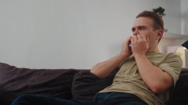 Adam kasvetli bir şekilde televizyon izliyor, içeriği tüketerek pasif eğlenceye dalıyor. Kavramsal Eğlence, Bağlantı Kesme ve Dinlenme, Bilgi Akımı, Duygusal Tepki