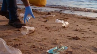 Bir adam sabahın erken saatlerinde plajdan plastik çöpleri topluyor. Çevre Koruma, Sorumluluk, Çevre Bilinci kavramı