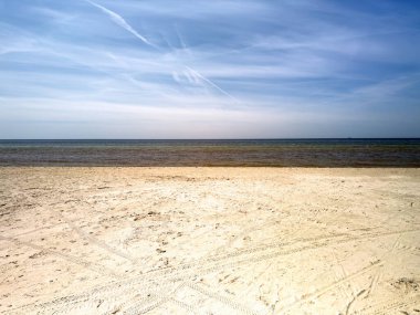 Açık mavi gökyüzü ve birkaç bulutu olan bir sahil.