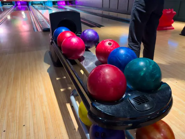 Akşamları parlayan ışıklarla dolu canlı bir bowling salonunda kullanıma hazır çeşitli renkli bovling topları bir askıda düzgünce düzenlenir..