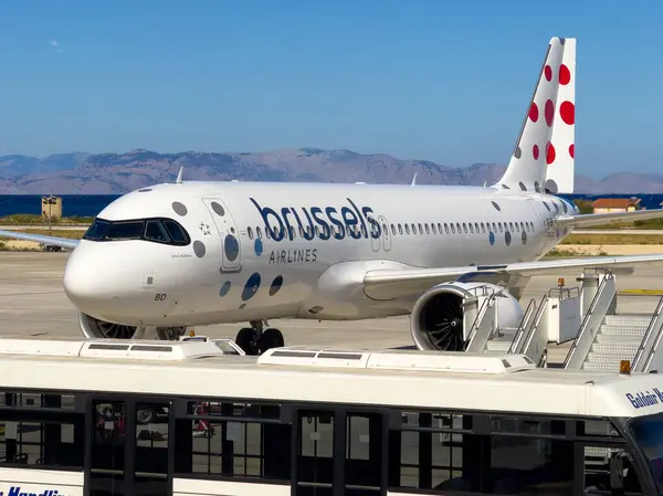 Bir Brüksel Havayolları Airbus A320 havaalanının pistinde, üzerinde dağlar ve üzerinde parlak mavi bir gökyüzü bulunan sakin bir manzarayla oturmaktadır..