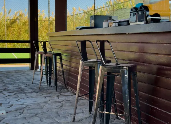 Konuklar, metal taburelerin yer aldığı büyüleyici bir açık hava barda toplanıyor. Yakınlardaki canlı bir spor sahasına bakarken güneşin tadını çıkarıyorlar. Mükemmel bir boş yer..