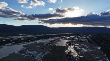 Zaman aşımı videosu, bulutların drone görüntüsü, göl ve sel ovaları tepenin üstündeki rüzgar türbininin arkasında..