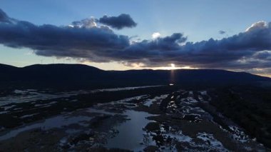4K drone videosu. Uçsuz bucaksız bir arazide nefes kesen bir gün batımı... dramatik gökyüzüne karşı siluetlerle dolu rüzgar türbinleri...