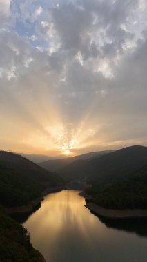 Sakin bir gölün üzerinde nefes kesici bir gün batımı, suyun üzerine altın ışınlar saçıyor.