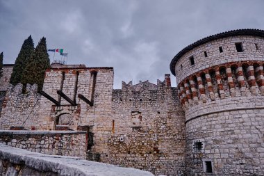 Kuvvetlendirilmiş Görkem: Brescia Şatosu 'nun Taş Duvarları ve İkonik Kuleleri Bulutlu Gök Altında