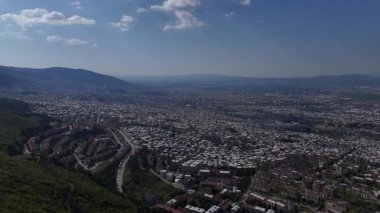 Bursa üzerinde süzülen ruhani bir İHA Verdant Hills 'ten geçen bir yol açıyor, Uzak Suların Yansıtıcı Huzuruna doğru, Doğanın Dinamik Gökyüzü Altında Açılan Şiirsel Dans.
