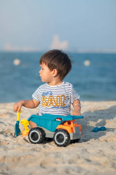 A toddler joyously plays with a toy vehicle on the beach, taking in the wonders of childhood by the sea. Baby boy playing on the beach with a toy truck sitting on the sand
