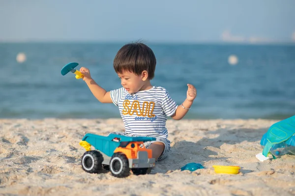 A toddler joyously plays with a toy vehicle on the beach, taking in the wonders of childhood by the sea. Baby boy playing on the beach with a toy truck sitting on the sand