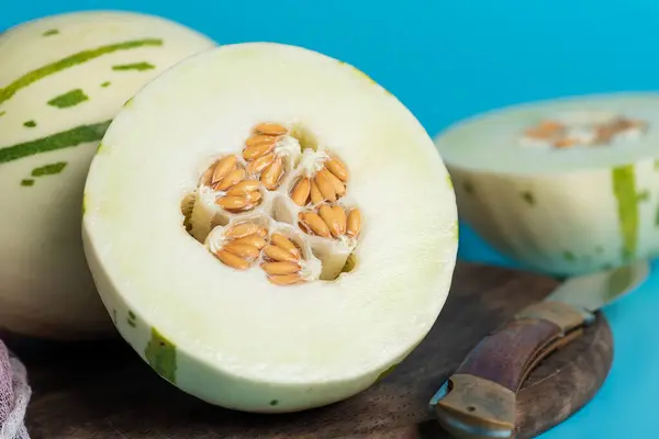 Ivory gaya melon with green dotted stripes and spots on a blue background. Colorful ripe juicy and soft fruit, sweet taste with floral notes. Whole and half melons on a wooden cutting board, close up