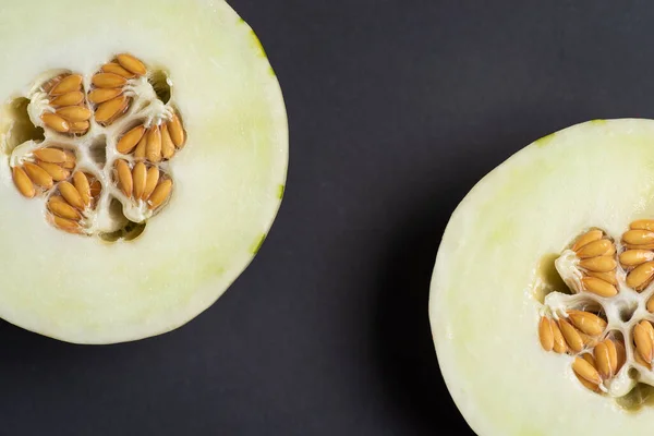 Ivory gaya melon with green dotted stripes and spots on a dark background. Colorful ripe, juicy and soft fruit, sweet taste with floral notes. Melon halves with yellow seeds in the middle