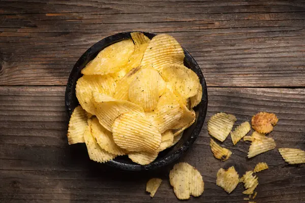 Crispy potato chips in a bowl on a wooden background