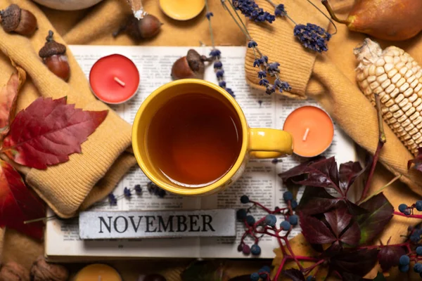 Autumn theme with autumn fruits and colors. A yellow sweater with a cup of tea on it, a book, autumn leaves, small scented candles and various fruits. Month November abstract background