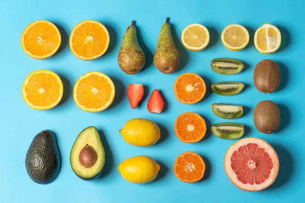 Colorful fruit juicy pattern on light blue background made of fresh tropical fruits - lemon, orange, kiwi, strawberry, grapefruit, pear and avocado