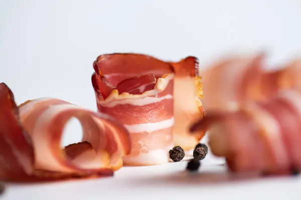 Rolled smoked bacon and a few peppercorns on a white background, close up. With copy space