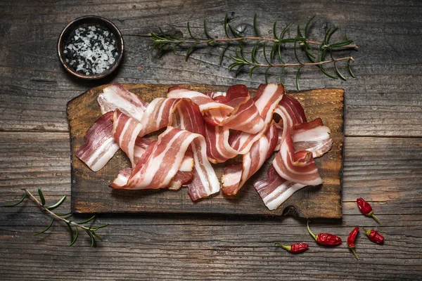 Rolled smoked bacon on a cutting board, with different spices on a wooden background
