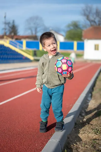 Ένα Χαρούμενο Αγοράκι Κρατάει Μια Ζωντανή Μπάλα Ποδοσφαίρου Στην Πίστα Royalty Free Φωτογραφίες Αρχείου