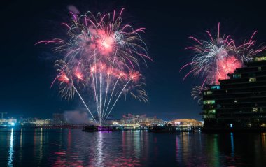 Fireworks illuminating the night sky as they reflect off the placid waters of Yas Island's seafront in Abu Dhabi, UAE. Fireworks usually take place on New Year's Eve, National Day, Eid festival, etc clipart