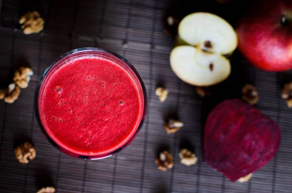 Koyu, ahşap arka planda pancar, havuç, elma ve cevizden yapılmış taze vejetaryen kırmızı smoothie.