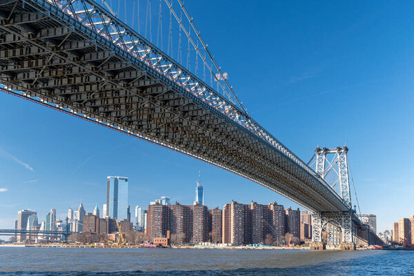 Bottom view of Williamsburg Bridge across the east river during a sunny morning, New York