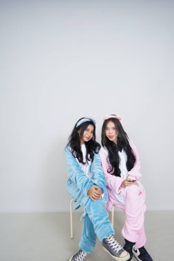 İki Asyalı genç kadın pijamalarıyla poz veriyor ve gülümsüyor.