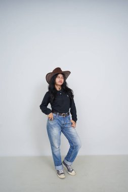 Şapkalı ve kot pantolonlu gri arka planda genç bir kız.