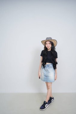 Şapkalı genç bir kadın, beyaz arka planda duruyor.