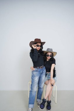 Siyah şapkalı, güneş gözlüklü ve kot pantolonlu iki güzel kadın.