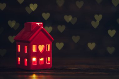 Candle holder. Ceramic tealight holder. Small red cozy house with windows. Light burning inside house. Bright red candle flame. Heart symbol of love. Home decoration. Happy St. Valentine's day