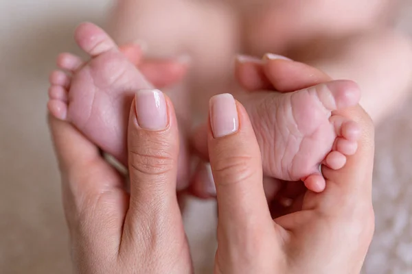 Newborn or Baby born. hild or kid feet in mother hand. New Mom or mother doing a massage. Barefoot baby. Happy woman. Kid toes. Woman hands love infant feet. Maternity hospital. Happy birthday.