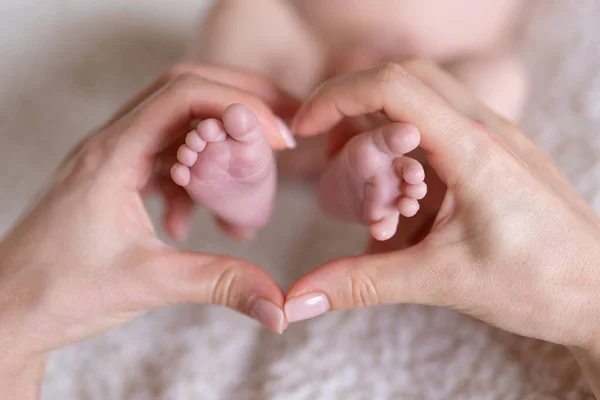 Newborn or Baby born. New Mom or mother doing Heart with fingers. Child or kid feet in mother hand. Barefoot baby. Happy woman. Kid toes. Woman hands love infant feet. Maternity hospital. Birthday