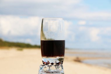 Gün batımında deniz kenarında ve kafede güzel bir bardakta kahverengi karbonatlı içecek. Kumsaldaki sıcakta soğuk köpüklü içecek..