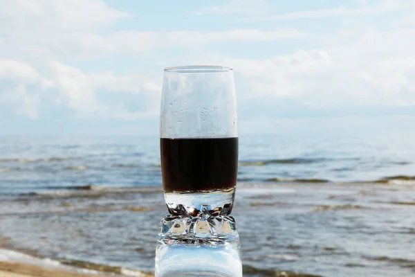 Brown carbonated drink in a beautiful glass at sunset by the sea and in a cafe. Cold frothy drink in the heat on the beach.
