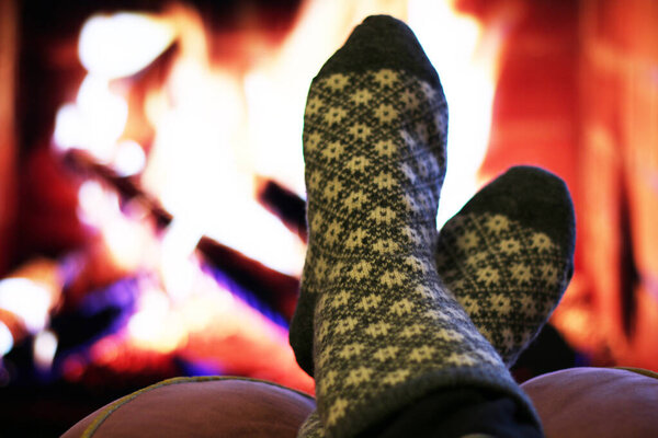 Men's feet in woolen socks warming themselves by the fireplace. A frozen man warms himself by the fireplace in winter.