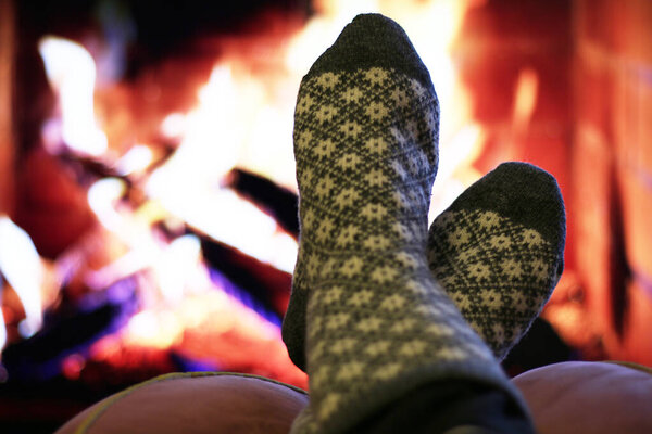 Men's feet in woolen socks warming themselves by the fireplace. A frozen man warms himself by the fireplace in winter.