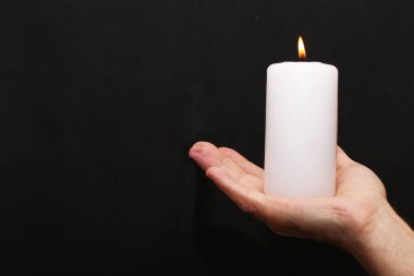 Bir adam elinde yanan beyaz bir mumu siyah bir arka planda tutuyor. Siyah bir arka planda elinde bir mum yanıyor..