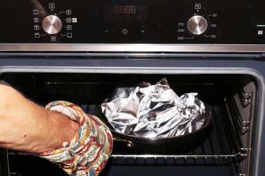 Eldivenli bir el, yemeği fırından çıkarır. Bir aşçının eli elektrikli fırını açar..