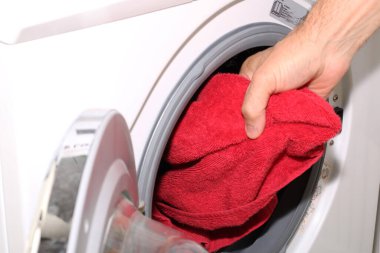 Bir el çamaşır makinesinden çamaşır çıkarır. Bir çamaşırcı, beyaz bir çamaşır makinesinden kırmızı çamaşırları çıkarıyor..