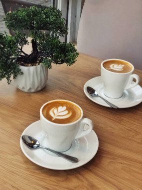 Krema köpüklü bir fincan kahve kaşıkla beyaz tabakta servis edilir. Kahve dükkanındaki ahşap bir masada birkaç tabak.. 