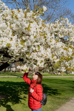 Bahar. Ağaçların çiçeklerle açtığı parkta bir kadın yürüyor..