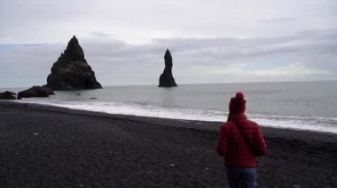 Kız siyah plaj boyunca yürüyor. İzlanda.