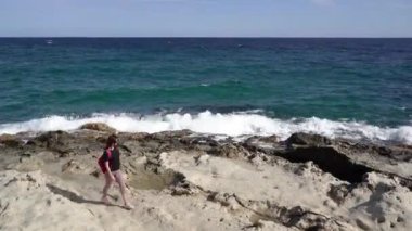 Resimli bir kayalık plajda bir kadın yürüyor..