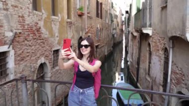 Venedik. Bir turist telefonuyla dar bir kanalın arka planında kendi fotoğrafını çeker..